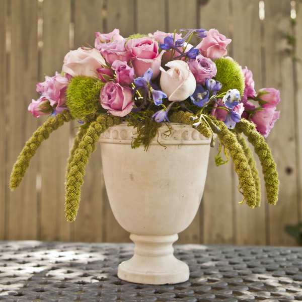 Pink and lavender roses arranged in a white pedestal vase