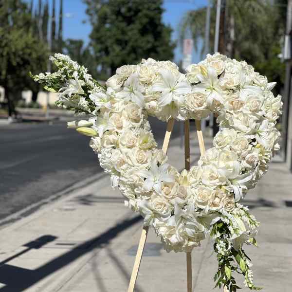 Heart-shaped white floral wreath on a wooden stand outdoors
