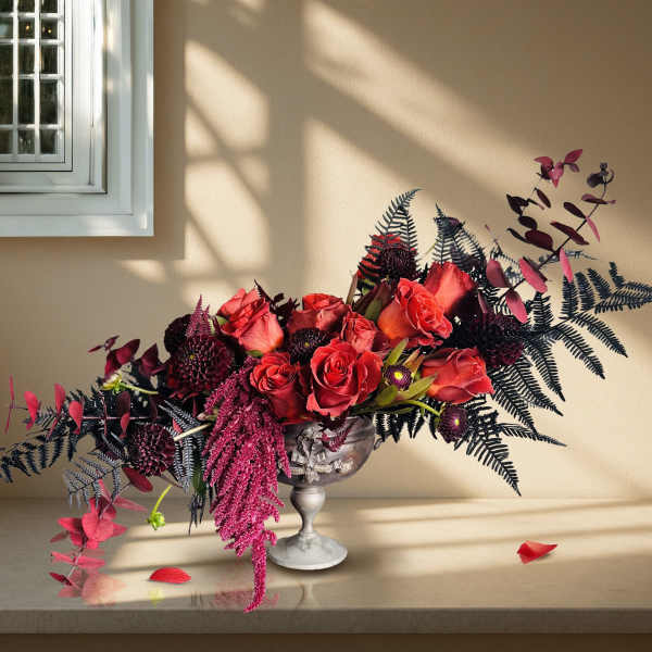 Red rose arrangement in a silver pedestal vase with dark foliage