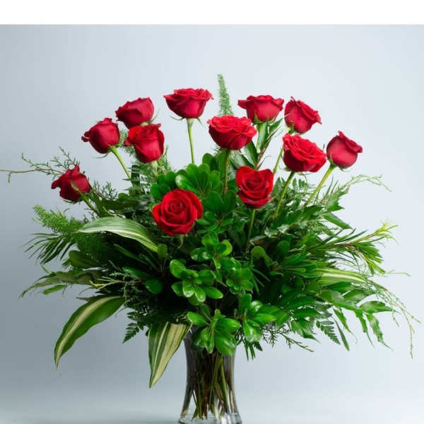 Red roses arranged in a clear glass vase with lush greenery