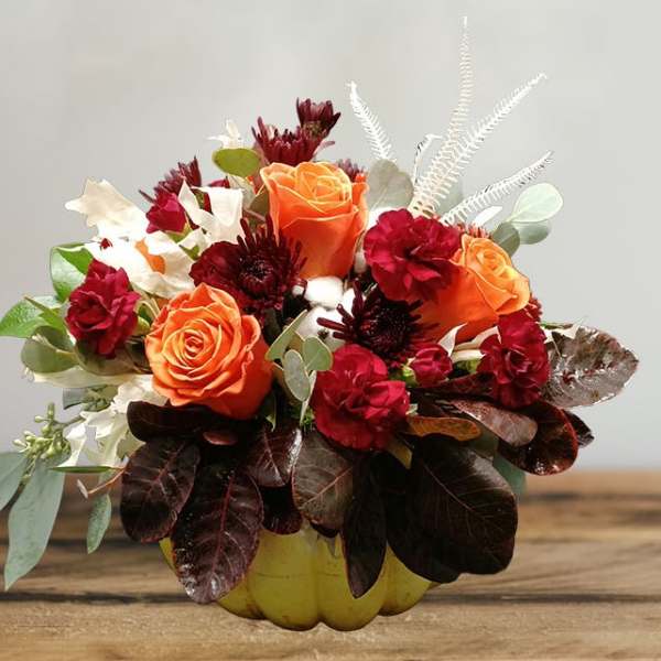 Orange and red rose arrangement in a yellow pumpkin container