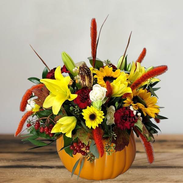 Fall floral arrangement in a pumpkin-shaped container with yellow lilies and sunflowers