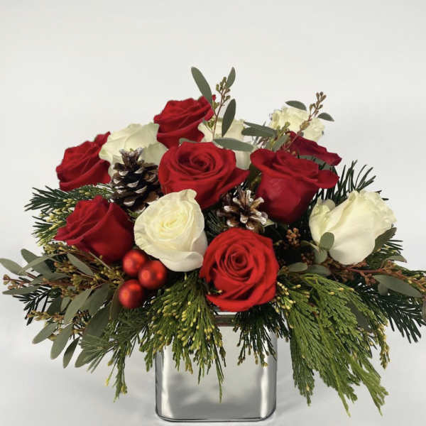 Red and white roses arranged in a square glass vase with pinecones and greenery