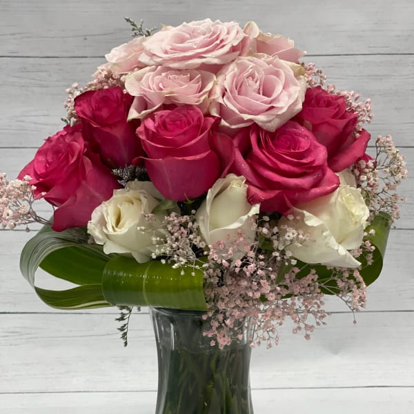 Pink and white roses arranged in a glass vase with pink filler flowers