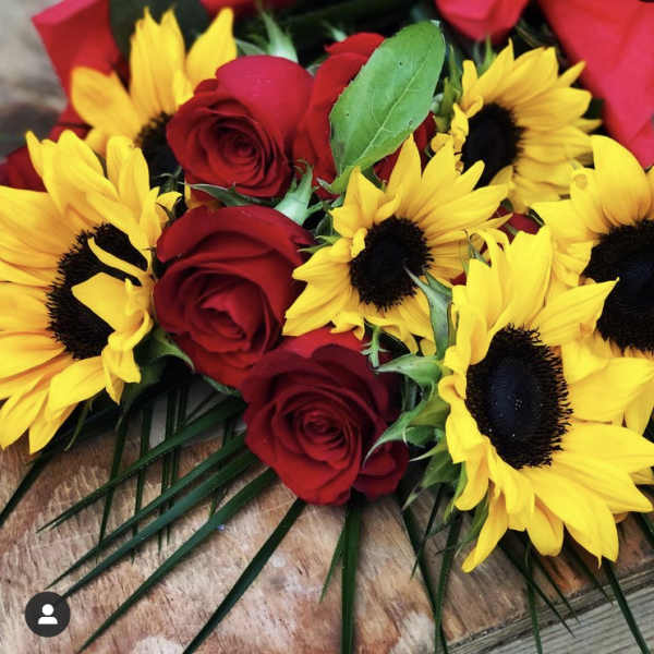 Bouquet of bright yellow sunflowers and red roses laid on a wooden surface