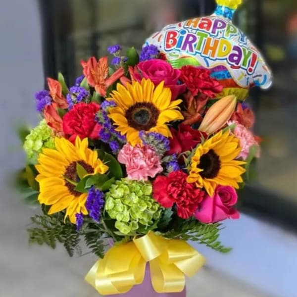 Colorful bouquet with sunflowers, roses, carnations, and a birthday balloon in a purple vase