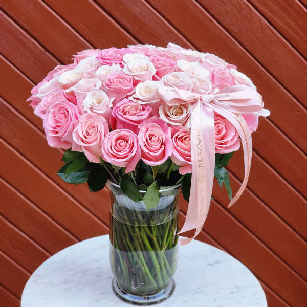 Pink and white roses arranged in a clear glass vase with a ribbon
