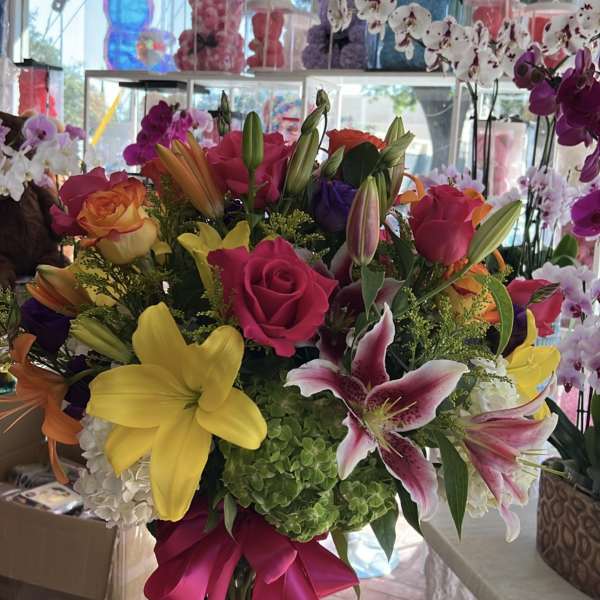 Colorful bouquet of roses and lilies with a pink ribbon in a glass vase