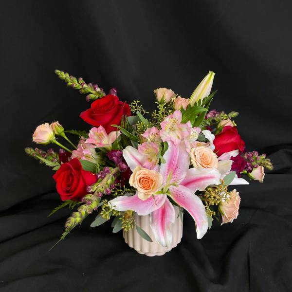 Mixed bouquet with pink lilies, red and peach roses in a white vase