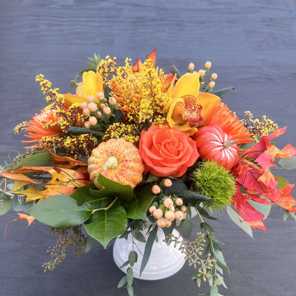 Autumn floral arrangement in a white vase with orange and yellow blooms