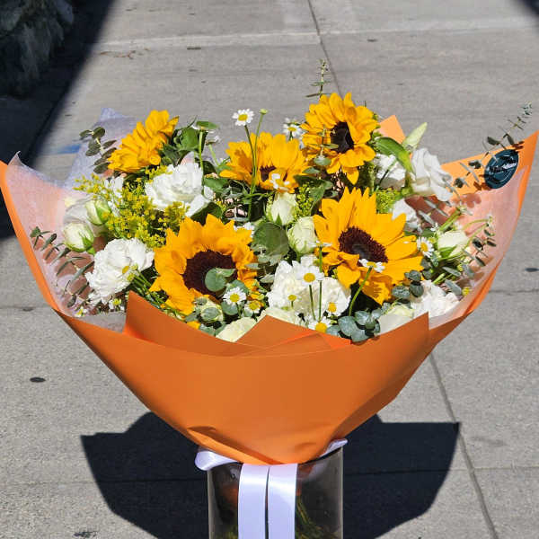 Bouquet of sunflowers and white flowers in orange wrap with a glass vase