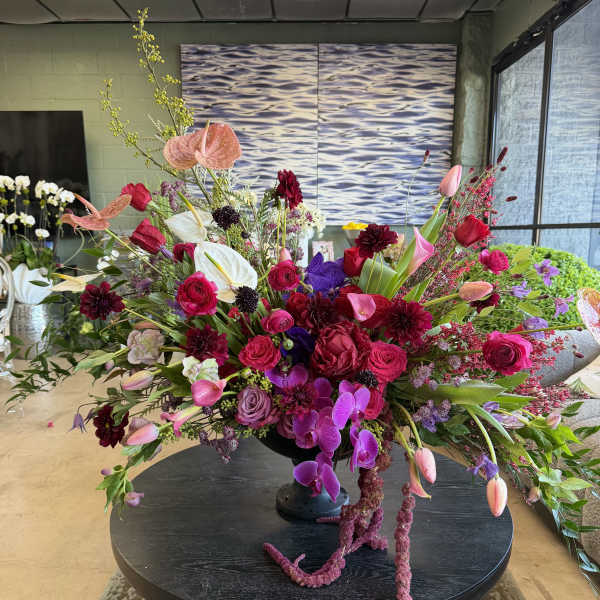 Large asymmetrical arrangement of pink, red, purple, and white flowers in a black pedestal vase on a round table