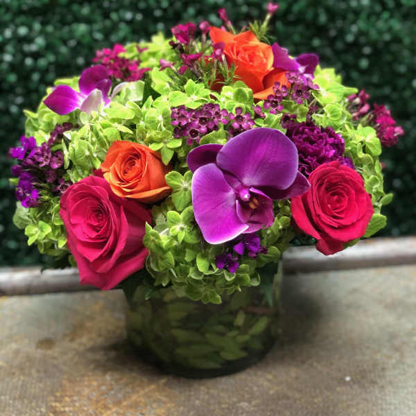 Round arrangement of bright roses, orchids, and green hydrangeas in a low glass vase