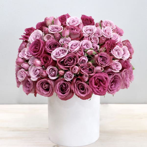 Dome-shaped arrangement of pink roses in a white cylinder vase