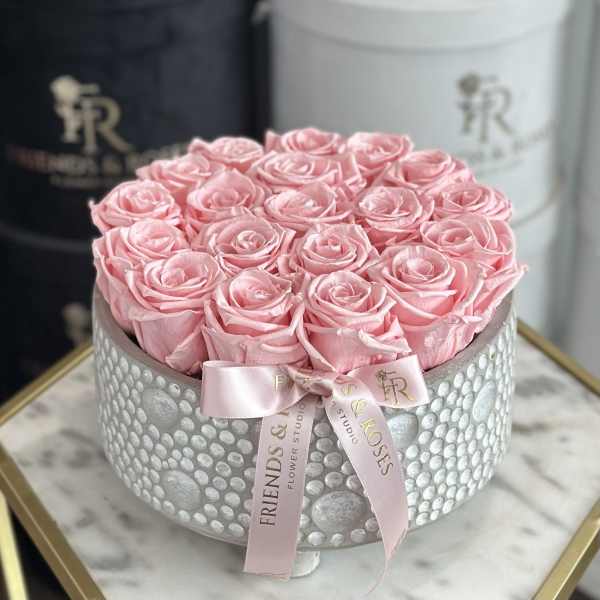 Pink roses arranged in a round silver box with a pink ribbon