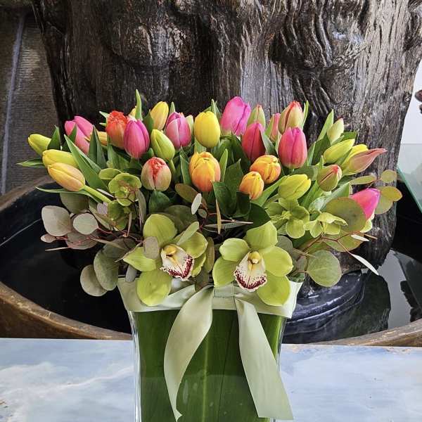 Colorful tulip bouquet with orchids in a glass vase