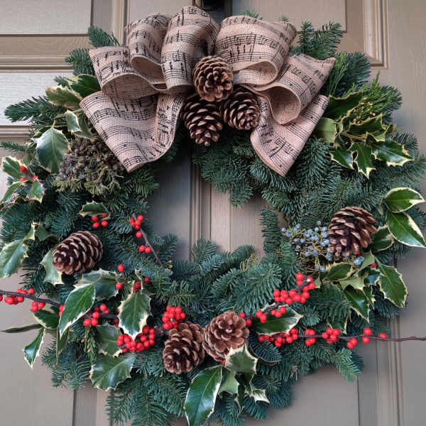 Holiday wreath with pine, holly, pinecones, and a music-note ribbon bow