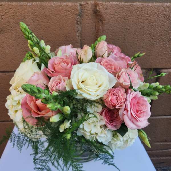 Round arrangement of pink and white roses with hydrangeas in a clear glass vase