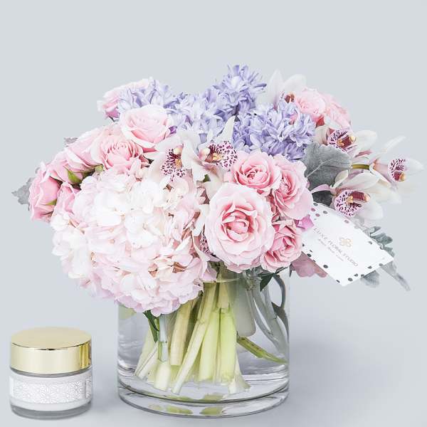 Pink and lavender bouquet in a clear glass vase with a small candle beside it