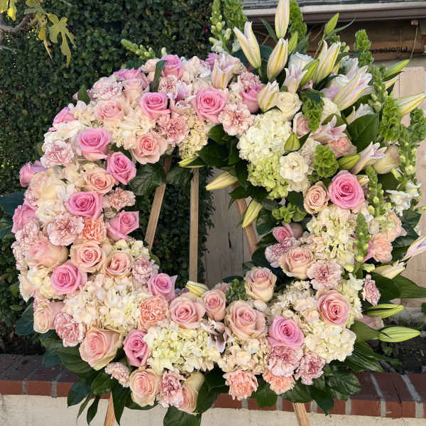 Large standing wreath of pink roses, white hydrangeas, carnations, and lilies on a wooden easel.