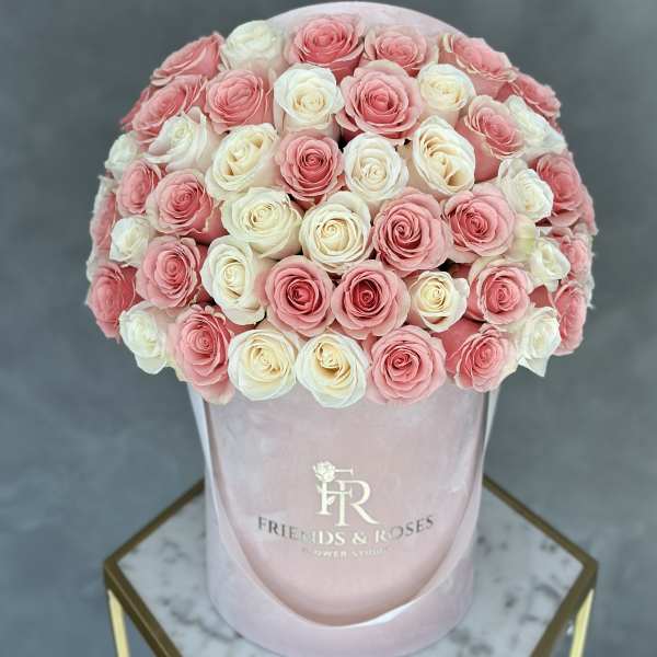 Pink and white roses arranged in a round hatbox.