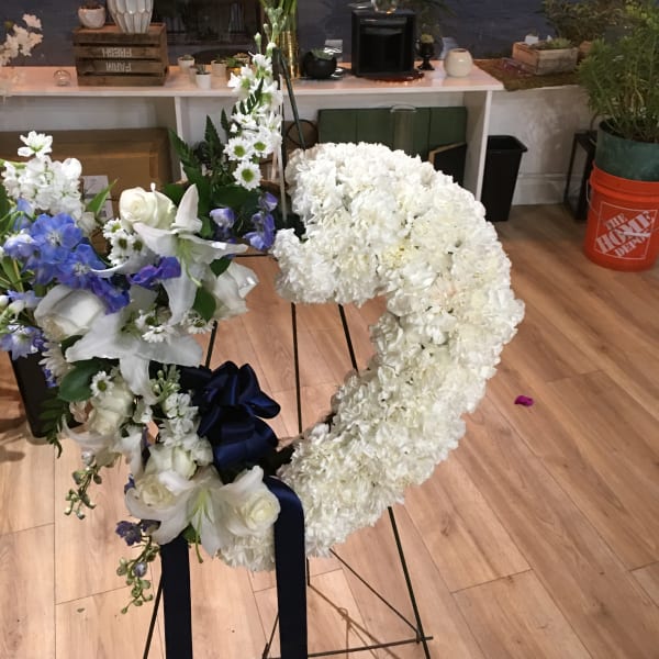 White floral wreath on a stand with blue and white flowers and a navy ribbon