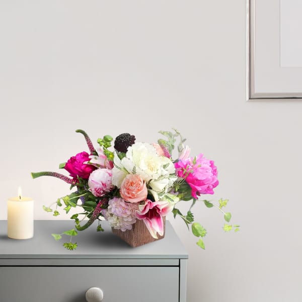 Pink and white floral arrangement in a square vase beside a candle