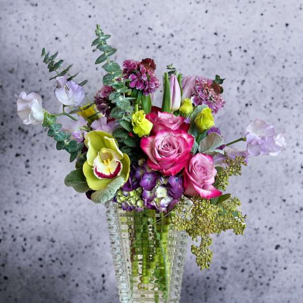 Mixed bouquet of pink roses, orchids, and calla lilies in a clear vase