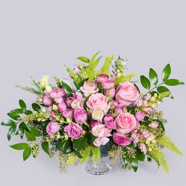 Low pink rose and ranunculus arrangement with snapdragons and bright green ferns in a clear glass vase