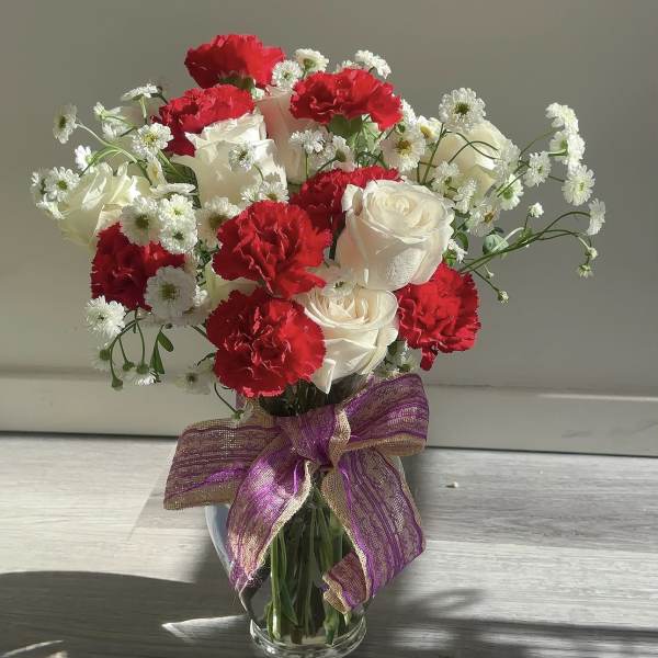 Bouquet of red carnations and white roses in a glass vase with a purple ribbon