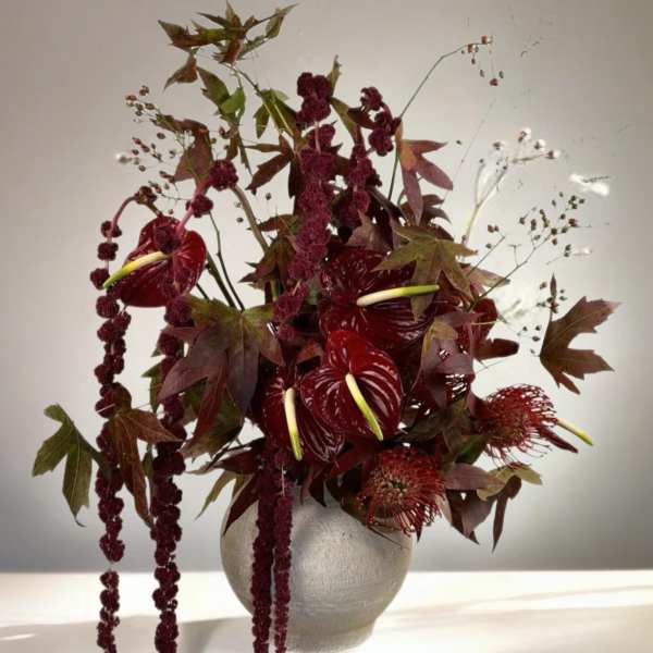 Deep red floral arrangement in a round vase with trailing burgundy blooms