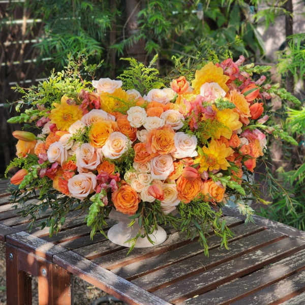 Large bouquet of peach, orange, and yellow flowers in a white pedestal vase