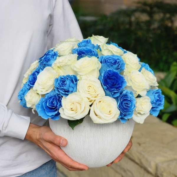 Blue and white roses arranged in a round white vase