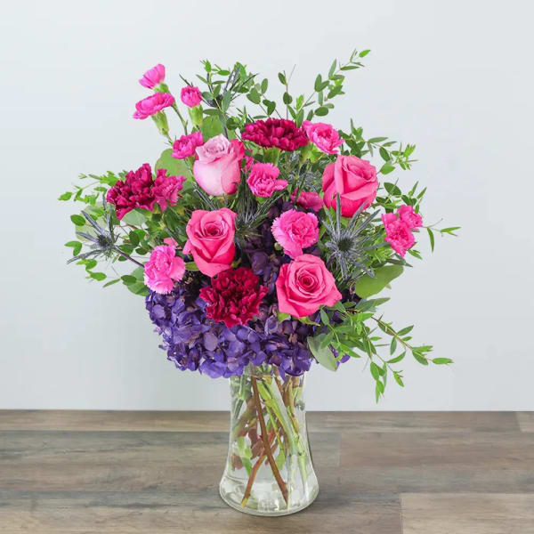 Pink roses and carnations in a clear glass vase with purple hydrangea