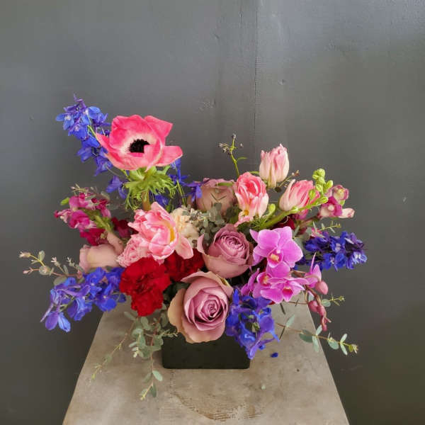 Mixed bouquet with pink roses, blue delphinium, and orchids in a black vase