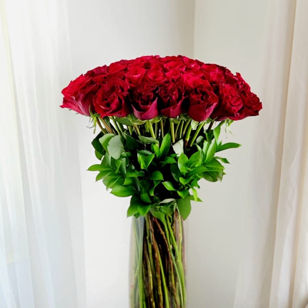 Tall vase of red roses with green foliage on a small table