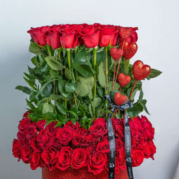 Red roses arranged in a glittery red box with heart picks