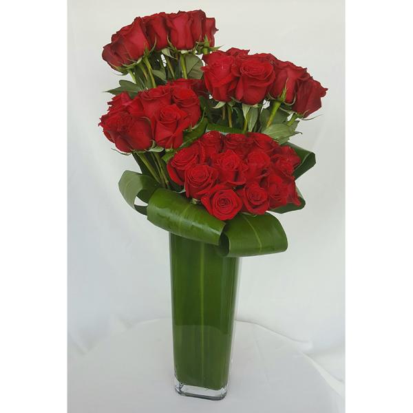 Red roses arranged in a tall green glass vase