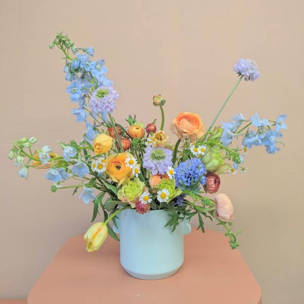 Pastel mixed bouquet in a light blue vase with blue and yellow blooms