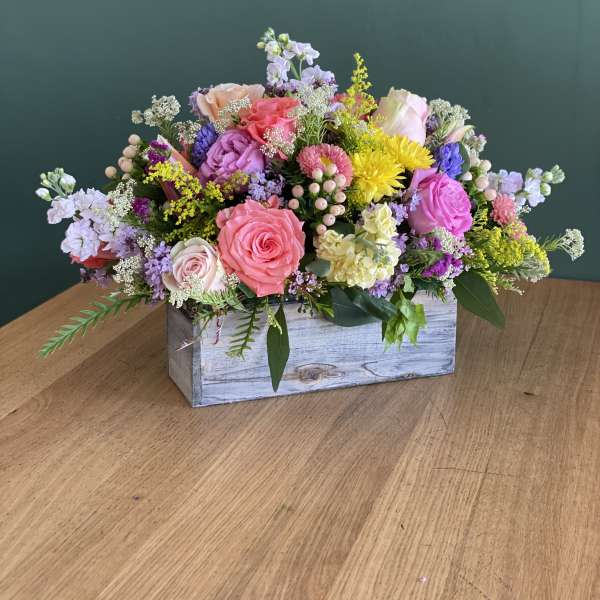 Mixed pink and purple flower arrangement in a wooden box