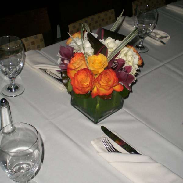 Table centerpiece with orange and purple flowers in a green glass vase