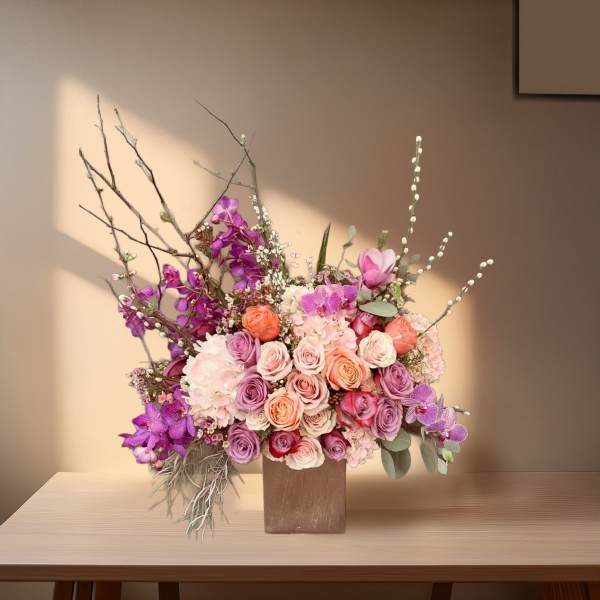 Mixed bouquet of pink, purple, and peach roses in a square vase