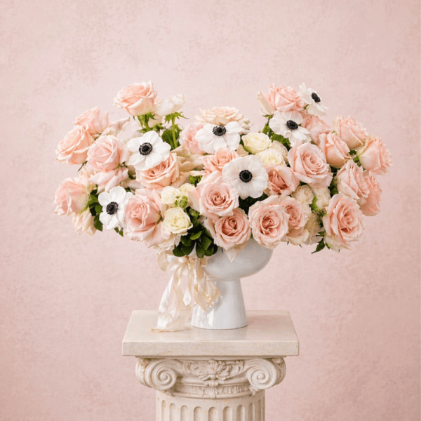 Blush roses and white anemones arranged in a white vase