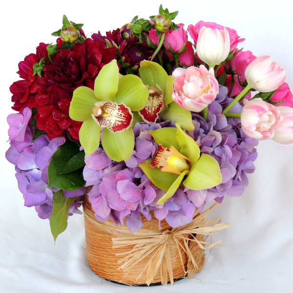 Mixed bouquet with orchids, hydrangeas, and tulips in a woven basket