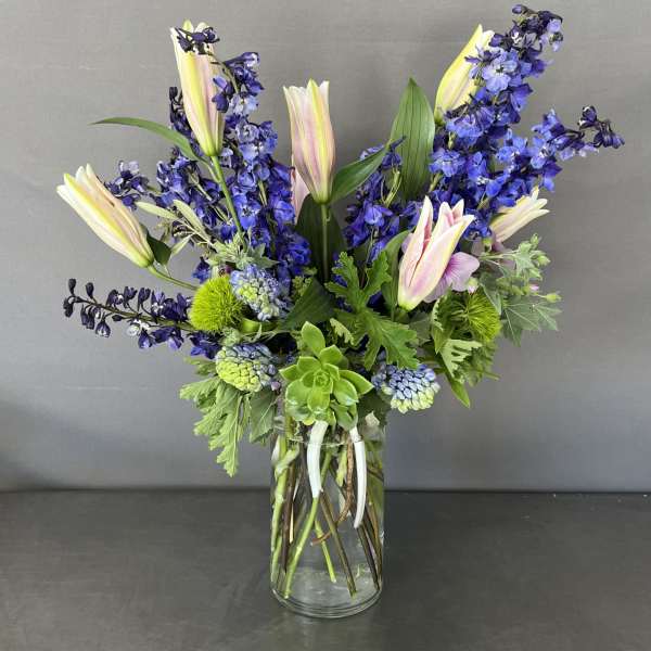 Tall bouquet of blue flowers and pale lilies in a clear glass vase