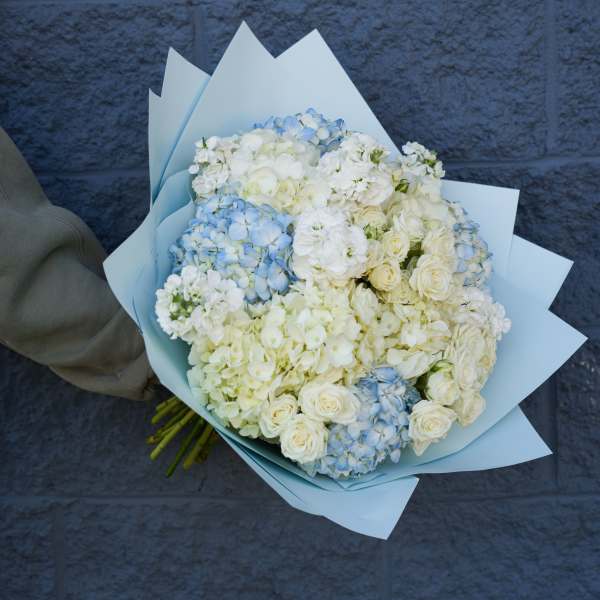 Bouquet of white and pale blue flowers wrapped in light blue paper