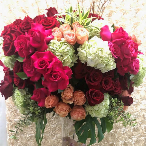 Tall bouquet of red, pink, peach, and white roses in a clear vase
