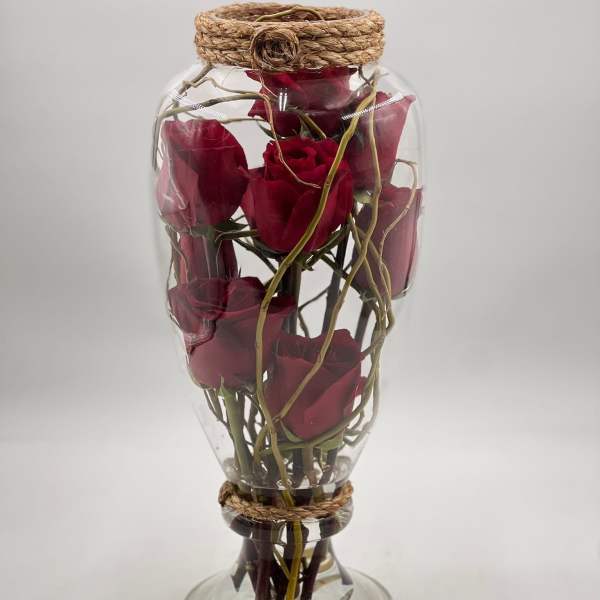 Tall clear glass jar filled with red roses and twigs, accented with rope wrapping.