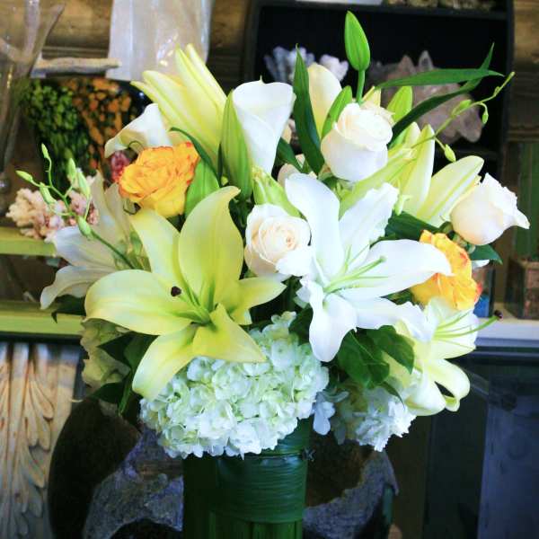 Bouquet of white lilies, white roses, and yellow roses in a tall green vase