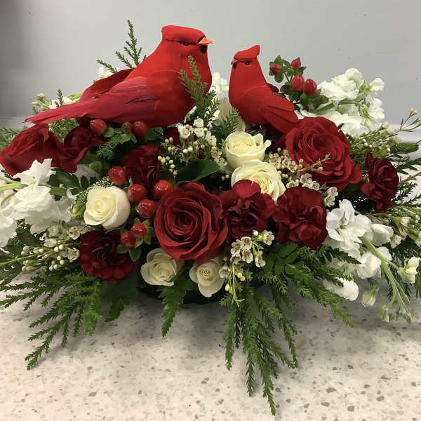 Red cardinal figurines sit in a red and white floral arrangement with roses.